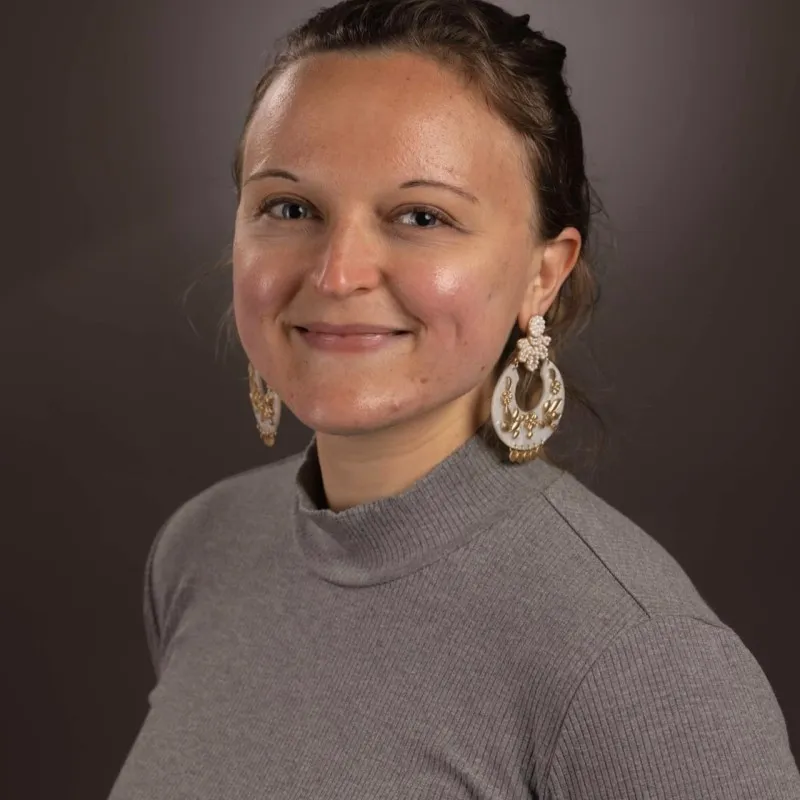 Portrait of Megan Bennett in a grey mock-neck top with statement earrings